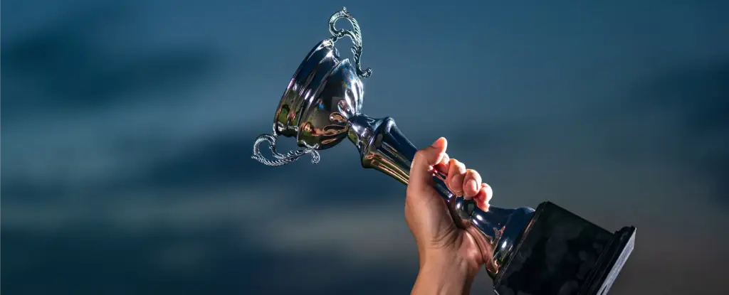 Een hand houdt triomfantelijk een glanzende zilveren trofee omhoog tegen een donkerblauwe lucht, wat een gevoel van voldoening en overwinning uitstraalt.