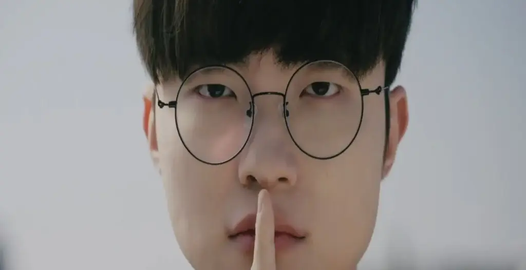 Een persoon met een bril vraagt met een gebaar om stilte door een vinger tegen zijn lippen te leggen. Hij kijkt ernstig en staat tegen een wazige stedelijke achtergrond.