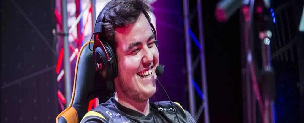 Iemand met een koptelefoon en een microfoon zit glimlachend in een gamingstoel. Hij of zij draagt een zwart-geel teamshirt met gaminglogo’s.